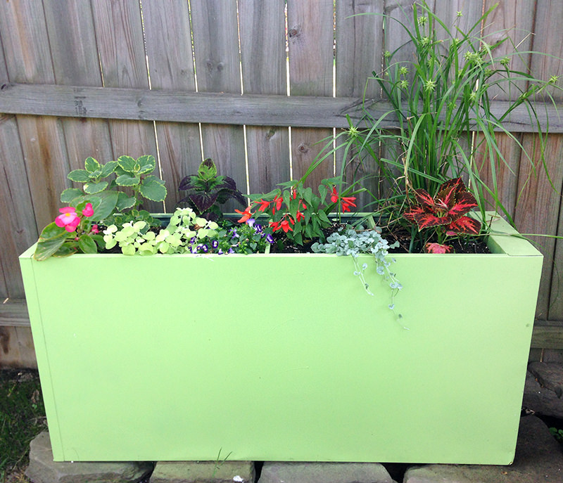 a green filing cabinet planter on the rocks with different plants is one of the best DIY planter ideas. 